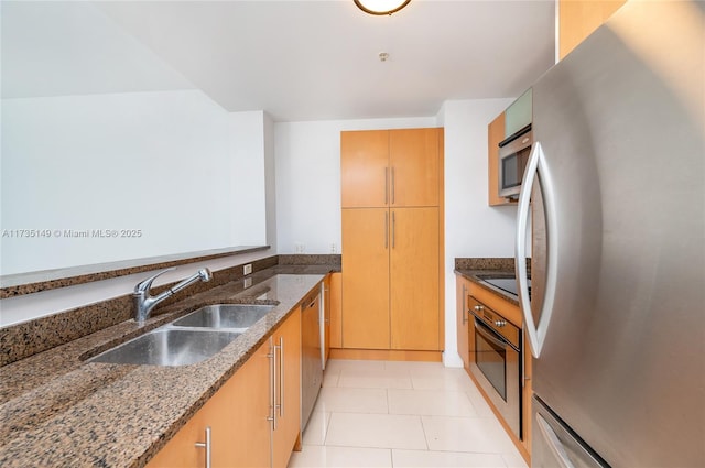 kitchen featuring appliances with stainless steel finishes, sink, light tile patterned floors, and dark stone counters