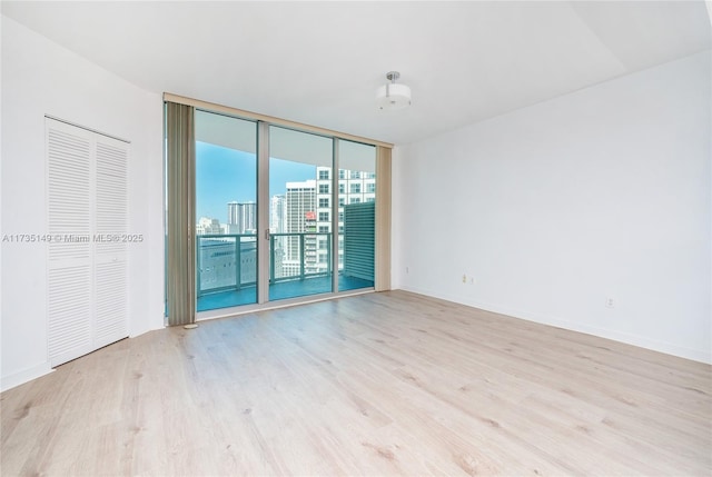 spare room with a wall of windows and light hardwood / wood-style floors