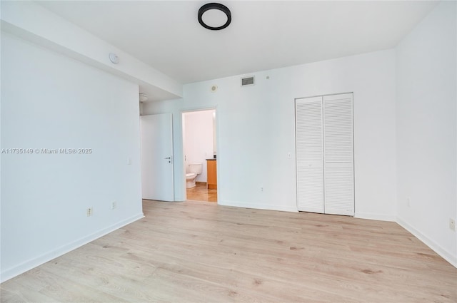 unfurnished bedroom featuring a closet, connected bathroom, and light hardwood / wood-style flooring