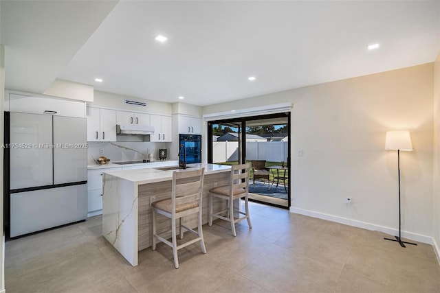 kitchen featuring a kitchen bar, sink, white cabinetry, refrigerator, and an island with sink