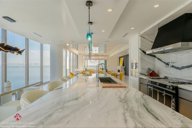 kitchen with sink, a water view, ventilation hood, light stone countertops, and decorative light fixtures