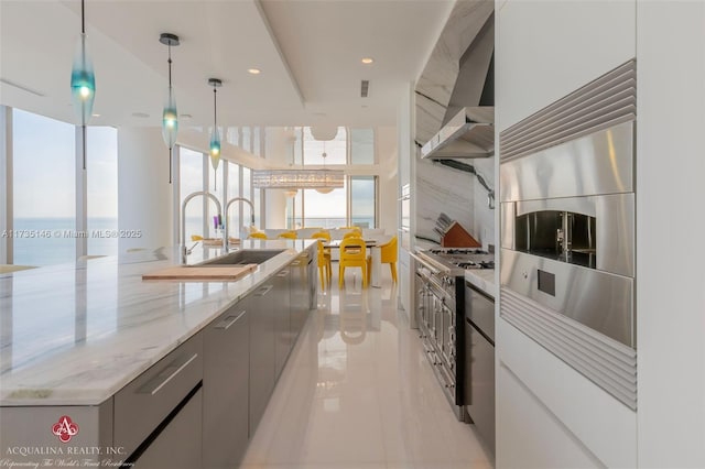 kitchen with sink, stainless steel gas range oven, a water view, decorative light fixtures, and wall chimney range hood