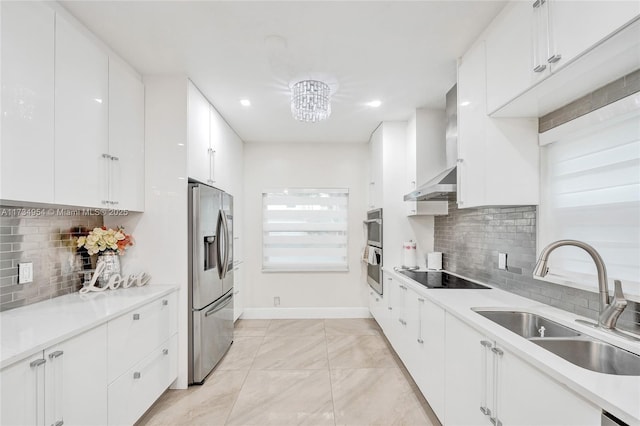 kitchen featuring baseboards, wall chimney exhaust hood, white cabinetry, a sink, and stainless steel appliances