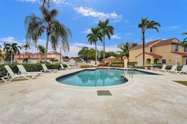 community pool with a patio area, fence, and a residential view