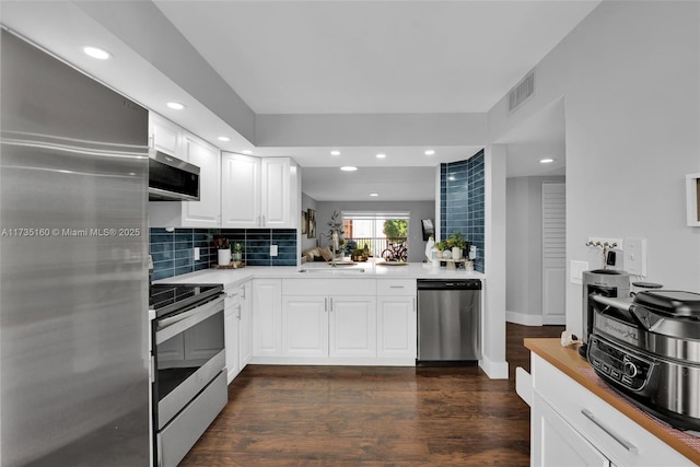 kitchen with white cabinetry, tasteful backsplash, appliances with stainless steel finishes, dark hardwood / wood-style flooring, and kitchen peninsula