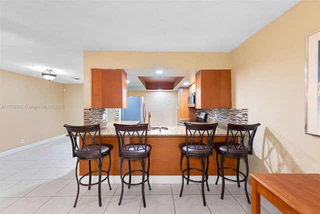 kitchen with stainless steel appliances, kitchen peninsula, decorative backsplash, and a breakfast bar area