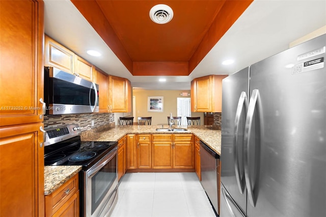 kitchen featuring sink, appliances with stainless steel finishes, a tray ceiling, kitchen peninsula, and light stone countertops