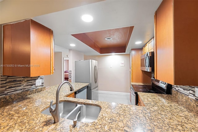 kitchen with light stone counters, appliances with stainless steel finishes, a raised ceiling, and sink