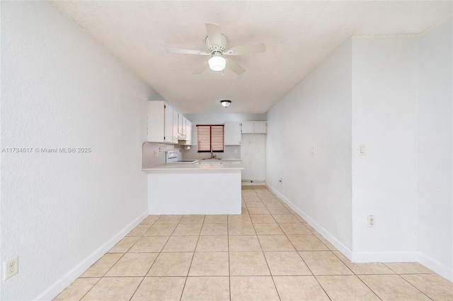 kitchen with light tile patterned floors, kitchen peninsula, white cabinets, ceiling fan, and stove