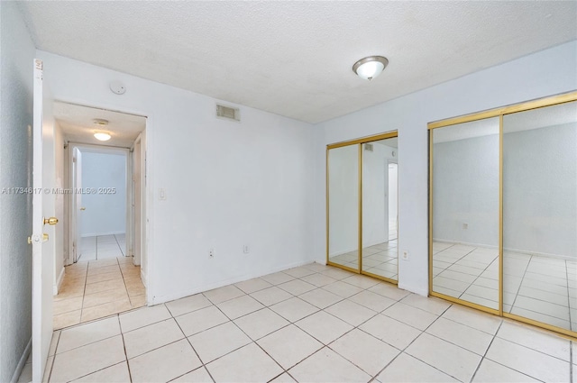 unfurnished bedroom with multiple closets, light tile patterned flooring, and a textured ceiling