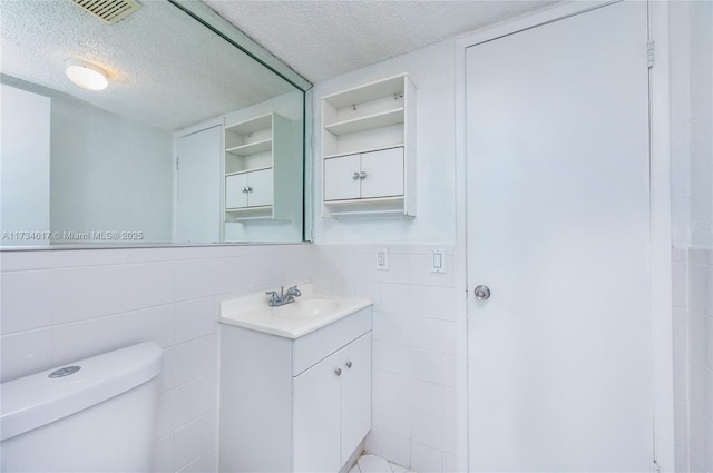 bathroom featuring vanity, tile walls, a textured ceiling, and toilet