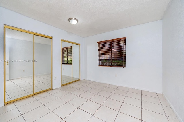 unfurnished bedroom with light tile patterned floors, a textured ceiling, and two closets