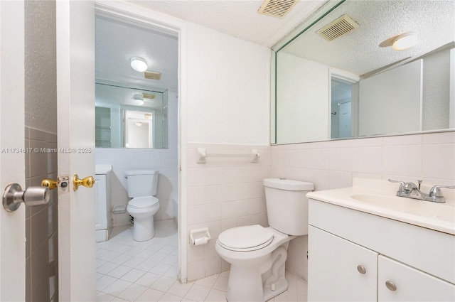 bathroom featuring vanity, toilet, a textured ceiling, and tile walls