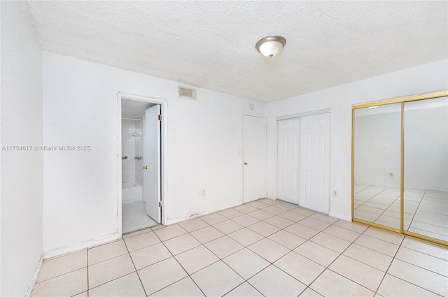 unfurnished bedroom featuring light tile patterned floors, two closets, ensuite bath, and a textured ceiling