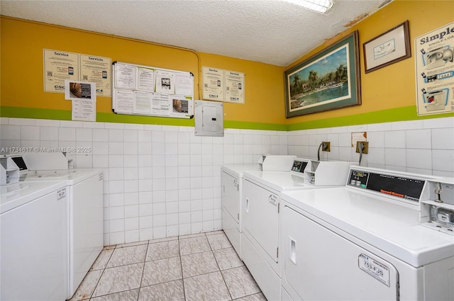 laundry area featuring light tile patterned flooring, a textured ceiling, tile walls, electric panel, and washing machine and dryer