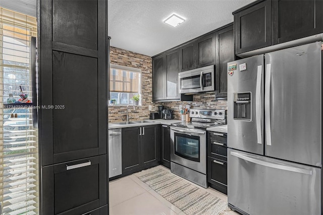 kitchen featuring sink, light tile patterned floors, backsplash, stainless steel appliances, and a textured ceiling