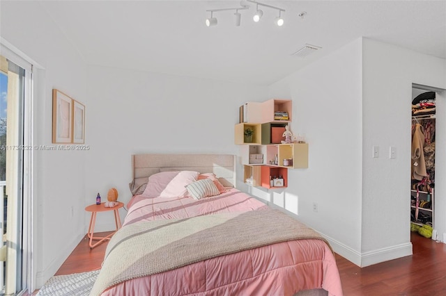 bedroom featuring a walk in closet, track lighting, dark hardwood / wood-style flooring, and a closet