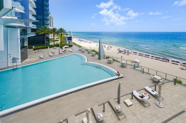 view of swimming pool featuring a patio, a water view, and a beach view