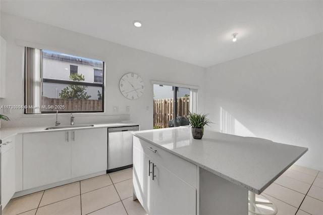 kitchen with a center island, light tile patterned floors, white cabinets, a sink, and dishwasher