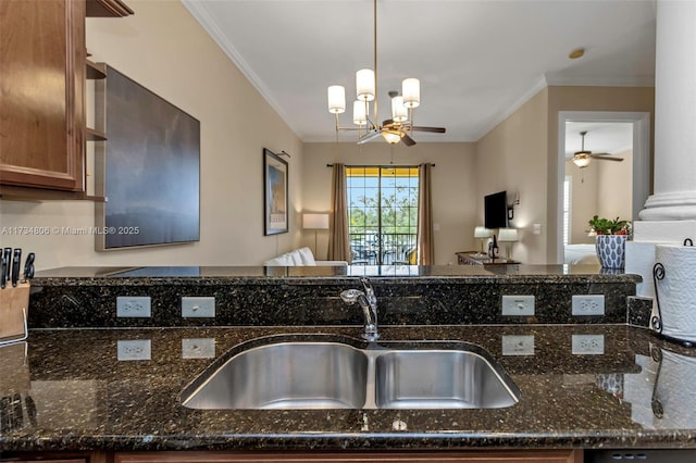 kitchen featuring sink, decorative light fixtures, ornamental molding, dark stone counters, and ceiling fan with notable chandelier