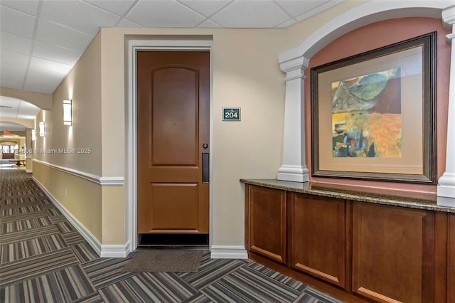 corridor featuring a paneled ceiling and dark carpet