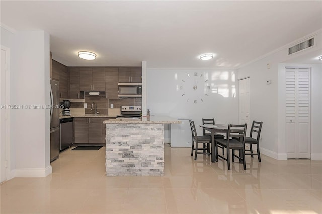 kitchen with sink, light tile patterned floors, appliances with stainless steel finishes, ornamental molding, and light stone countertops