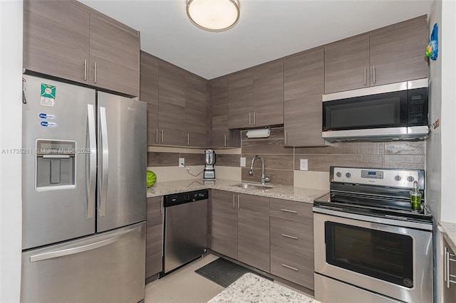 kitchen with sink, backsplash, light tile patterned floors, stainless steel appliances, and light stone countertops