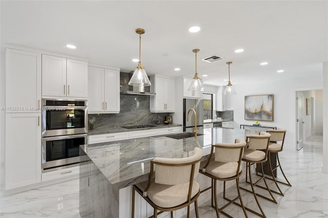 kitchen featuring appliances with stainless steel finishes, white cabinetry, a spacious island, light stone counters, and decorative light fixtures