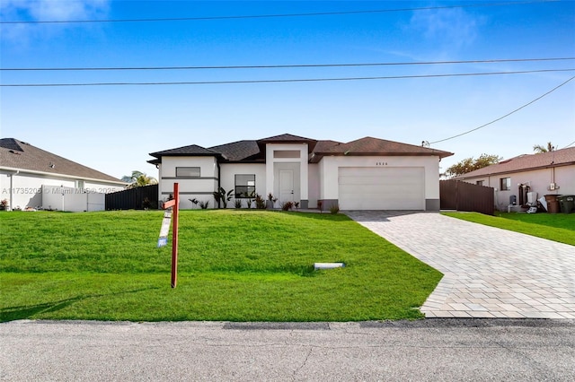 prairie-style home with fence, a front yard, stucco siding, decorative driveway, and a garage