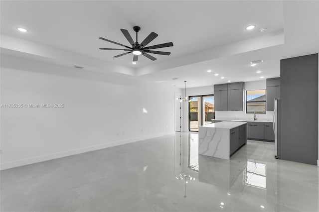 kitchen featuring gray cabinets, a spacious island, a tray ceiling, light stone countertops, and decorative light fixtures