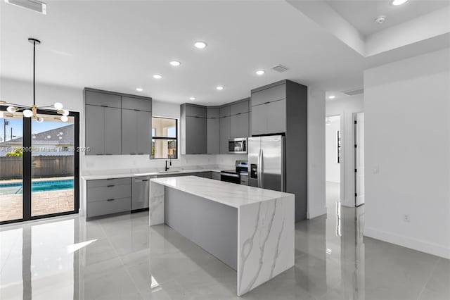 kitchen featuring pendant lighting, sink, stainless steel appliances, light stone countertops, and a kitchen island