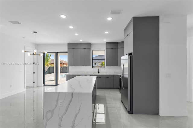 kitchen featuring a kitchen bar, a center island, hanging light fixtures, stainless steel refrigerator, and gray cabinets