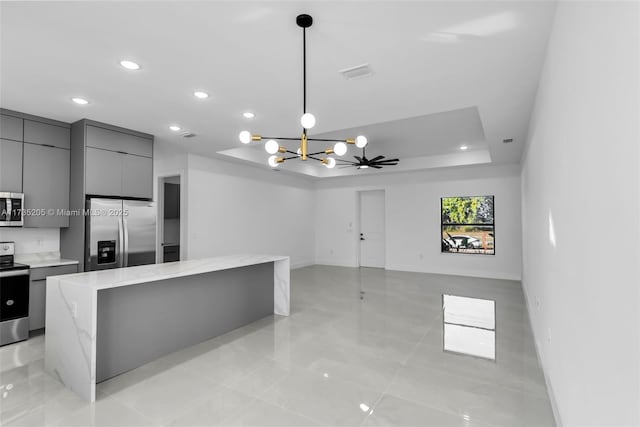 kitchen featuring appliances with stainless steel finishes, gray cabinetry, a kitchen island, decorative light fixtures, and a raised ceiling