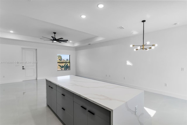 kitchen with ceiling fan with notable chandelier, decorative light fixtures, gray cabinetry, a tray ceiling, and light stone countertops