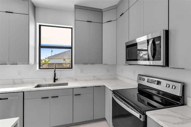 kitchen featuring stainless steel appliances, light stone countertops, sink, and gray cabinetry