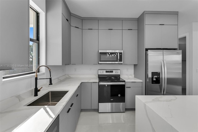 kitchen featuring stainless steel appliances, light stone countertops, sink, and gray cabinets