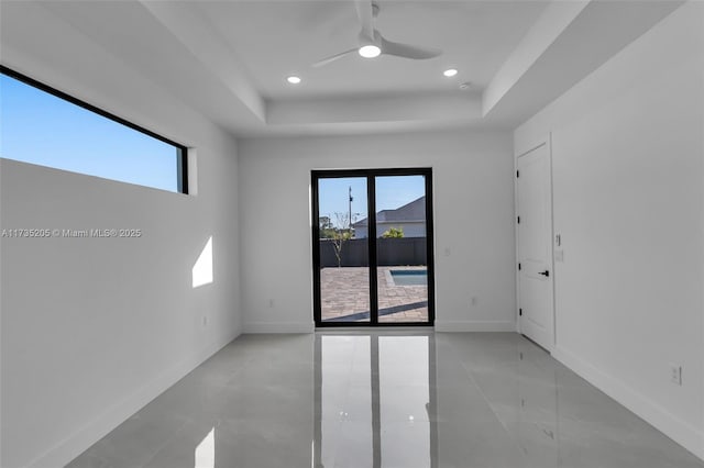 empty room with a wealth of natural light, ceiling fan, and a tray ceiling