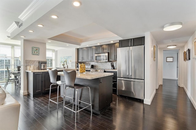 kitchen with tasteful backsplash, ornamental molding, stainless steel appliances, and a kitchen breakfast bar