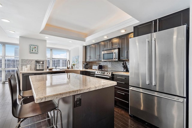 kitchen featuring a breakfast bar, a tray ceiling, kitchen peninsula, stainless steel appliances, and light stone countertops