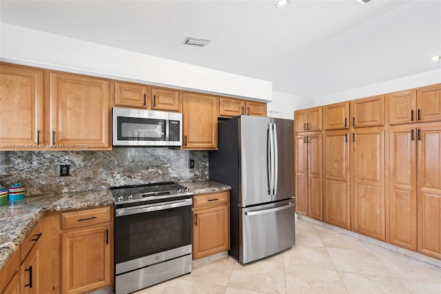 kitchen featuring stainless steel appliances, tasteful backsplash, dark stone countertops, and light tile patterned floors