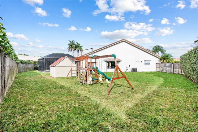 rear view of property with central AC unit, a playground, and a lawn