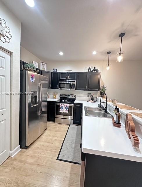 kitchen with sink, decorative light fixtures, stainless steel appliances, and light hardwood / wood-style floors