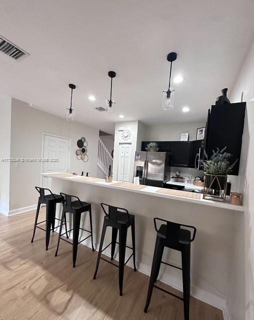 kitchen with decorative light fixtures, a breakfast bar area, and stainless steel refrigerator with ice dispenser