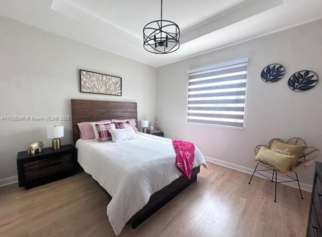 bedroom featuring a tray ceiling, a chandelier, and hardwood / wood-style floors