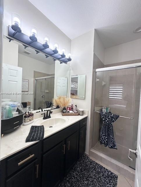 bathroom featuring tile patterned floors, vanity, a shower with shower door, and a textured ceiling