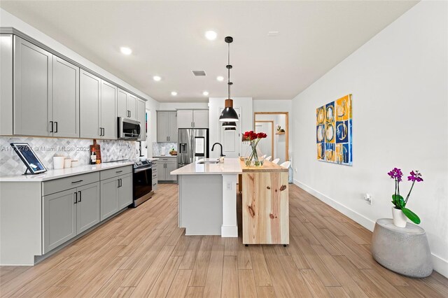 kitchen with appliances with stainless steel finishes, pendant lighting, tasteful backsplash, an island with sink, and gray cabinetry