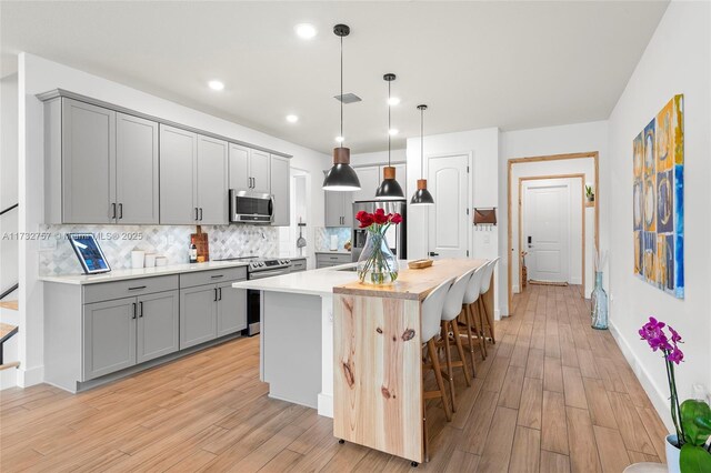 kitchen featuring a breakfast bar, a center island with sink, gray cabinets, pendant lighting, and stainless steel appliances