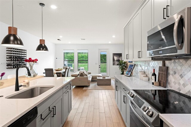 kitchen featuring decorative light fixtures, sink, stainless steel appliances, light stone countertops, and light wood-type flooring