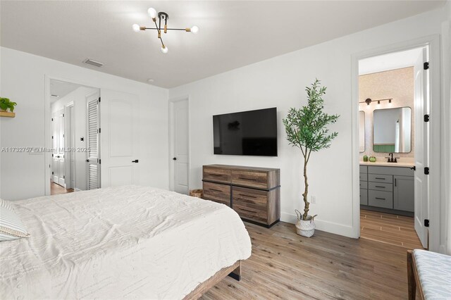 bedroom featuring an inviting chandelier, light hardwood / wood-style flooring, and ensuite bathroom