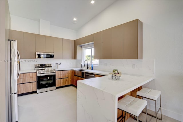 kitchen with sink, a breakfast bar area, appliances with stainless steel finishes, tasteful backsplash, and kitchen peninsula